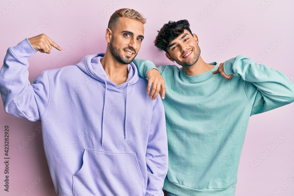 Homosexual gay couple standing together wearing casual clothes looking confident with smile on face, pointing oneself with fingers proud and happy. Homosexual gay couple standing together wearing casual clothes looking confident with smile on face, pointing oneself with fingers proud and happy.
