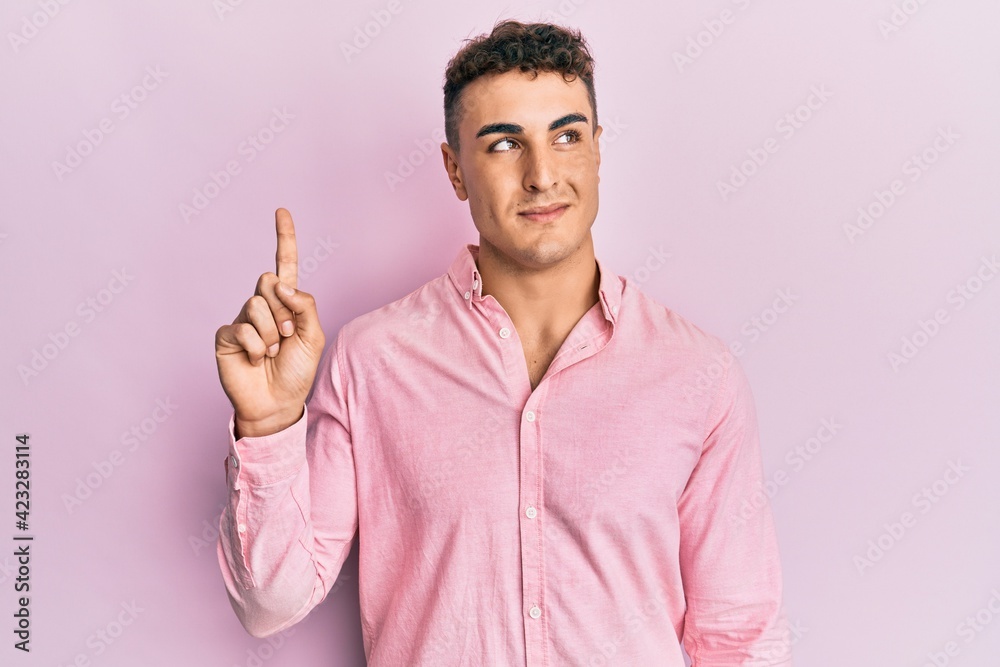 Hispanic young man pointing up with fingers smiling looking to the side and staring away thinking. Hispanic young man pointing up with fingers smiling looking to the side and staring away thinking.