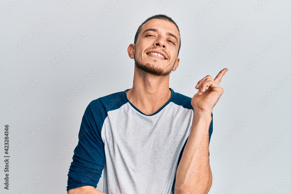 Hispanic young man wearing casual clothes with a big smile on face, pointing with hand and finger to the side looking at the camera. Hispanic young man wearing casual clothes with a big smile on face, pointing with hand and finger to the side looking at the camera.
