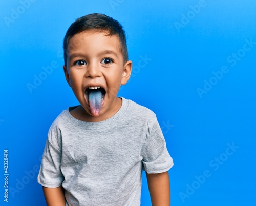 Adorable latin toddler showing blue tongue standing over isolated background. photo