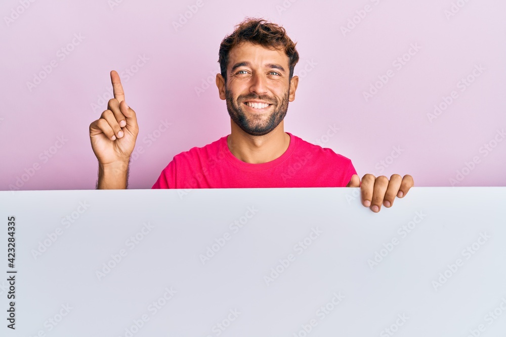 Handsome man with beard holding blank empty banner smiling happy pointing with hand and finger to the side Handsome man with beard holding blank empty banner smiling happy pointing with hand and finger to the side