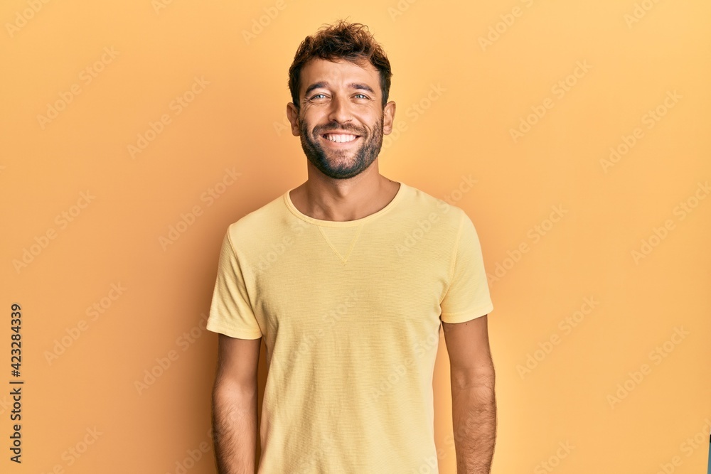 Handsome man with beard wearing casual yellow tshirt over yellow background with a happy and cool smile on face. lucky person. Handsome man with beard wearing casual yellow tshirt over yellow background with a happy and cool smile on face. lucky person.