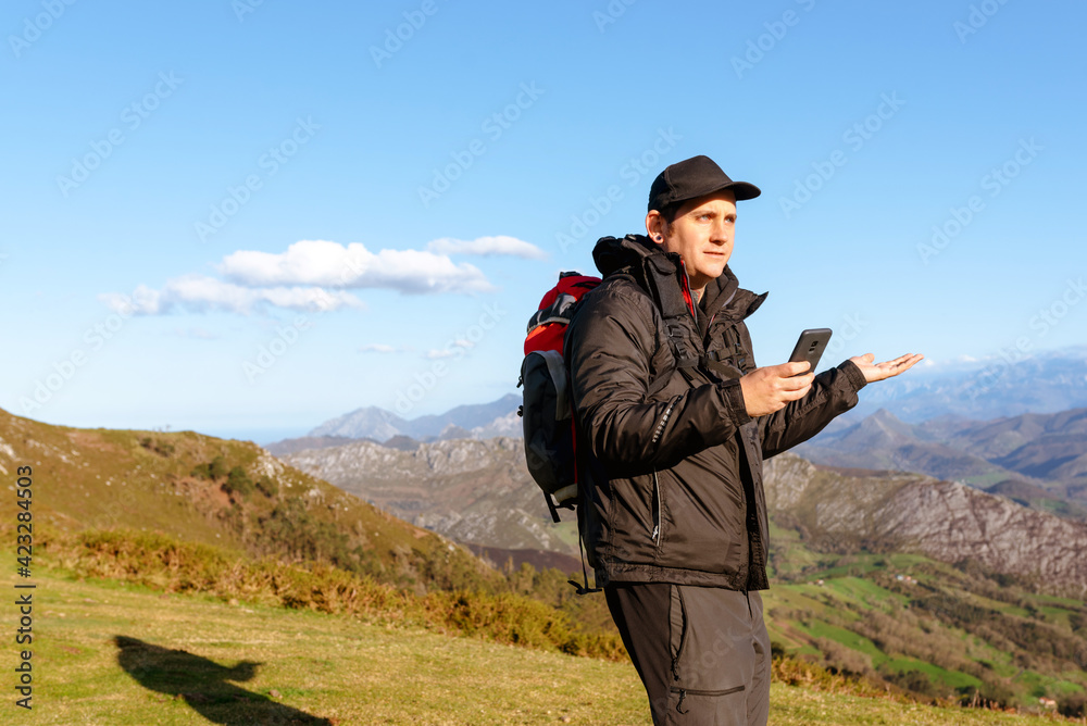 hiker making a lost gesture and using his mobile phone to guide himself on his route in nature. person using gps. Mountain Sports.