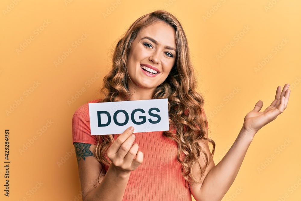 Young blonde girl holding paper with dogs message celebrating achievement with happy smile and winner expression with raised hand Young blonde girl holding paper with dogs message celebrating achievement with happy smile and winner expression with raised hand