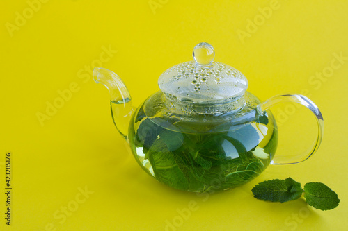 Mint tea in the glass teapot on the yellow background. Close-up. Copy space.
