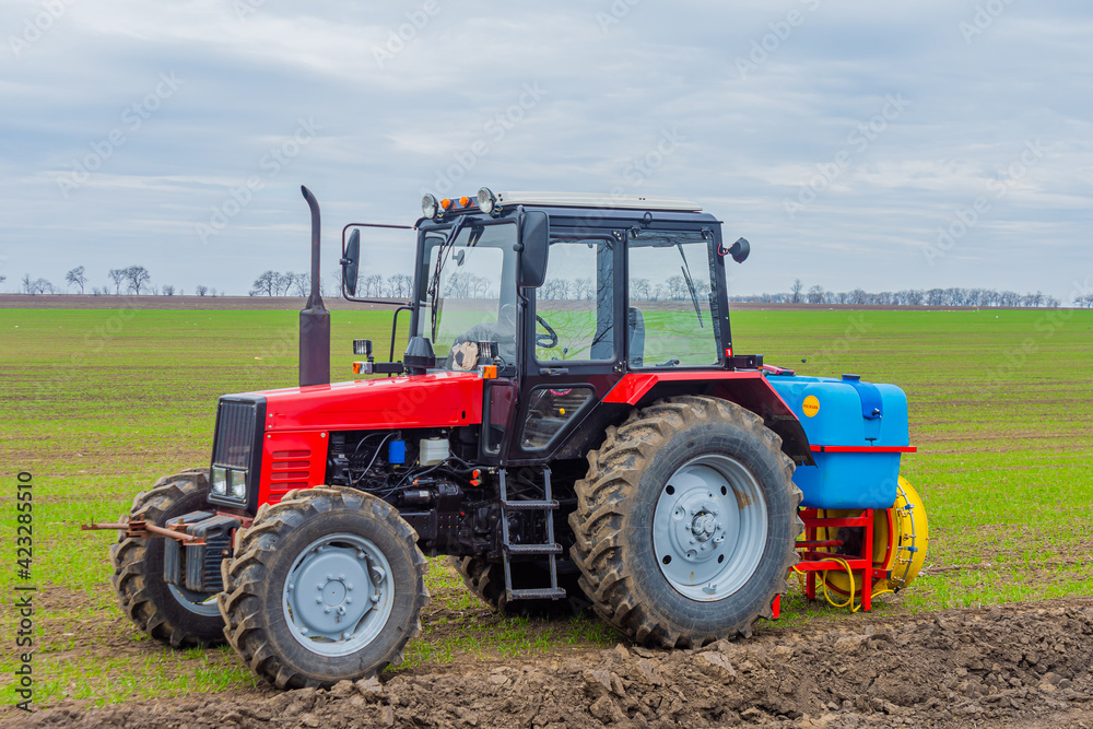 Agricultural tractor in the field with sown winter wheat. The tractor is designed to spray pesticides on crops. Agricultural tractor in the field with sown winter wheat. The tractor is designed to spray pesticides on crops.