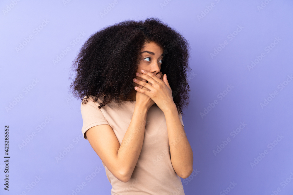 Young african american woman isolated on purple background covering mouth and looking to the side
