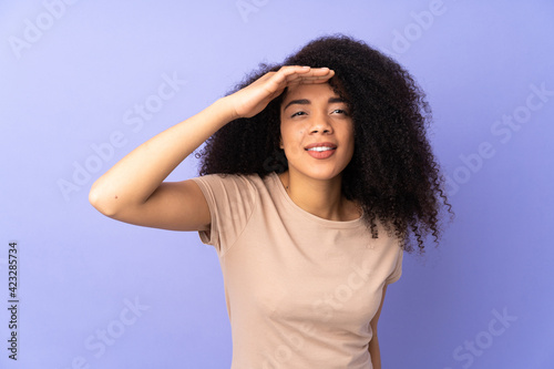 Young african american woman isolated on purple background looking far away with hand to look something