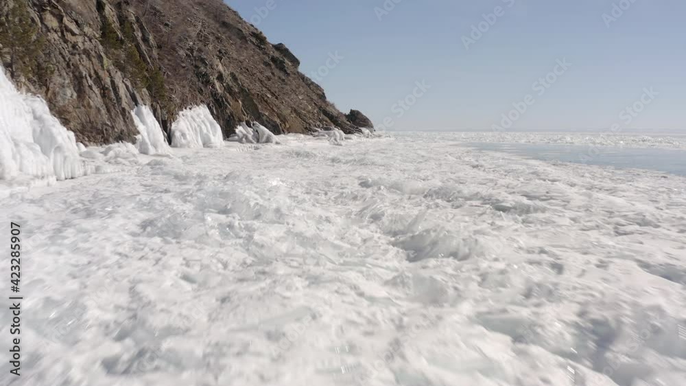 Flight in front of the rocky coast and the coastal area of Lake Baikal covered with ice hummocks. Ice blocks and impassable ice in winter on Lake Baikal. Flight in front of the rocky coast and the coastal area of Lake Baikal covered with ice hummocks. Ice blocks and impassable ice in winter on Lake Baikal.