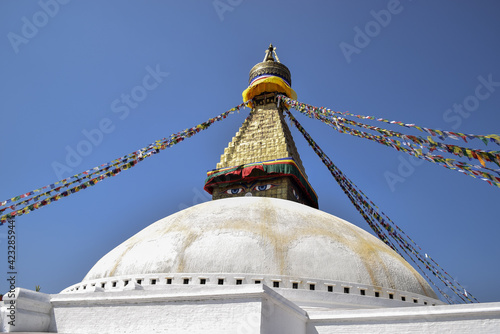The eyes of Boudhanath stupa and prayer flags hanging on it. It is a sunny day and the sky is blue. Kathmandu, Nepal.