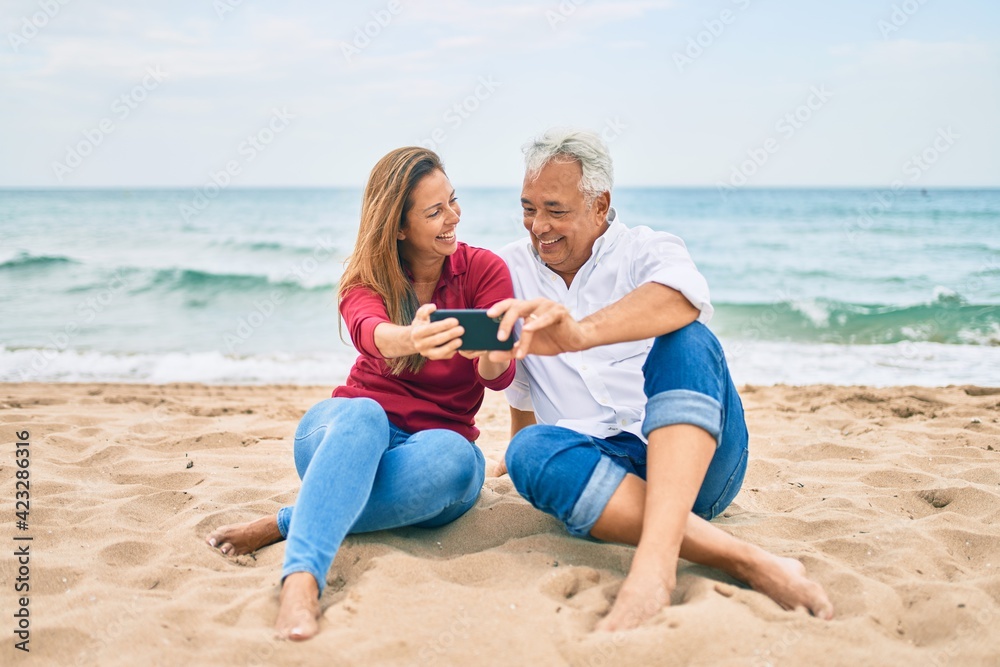 Middle age hispanic couple making selfie by the smartphone at the beach.