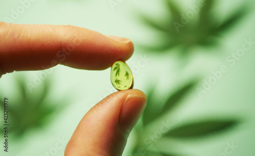 Close up hand holding CBD oil pill. Cannabis leaves reflection. Medical marijuana usage 