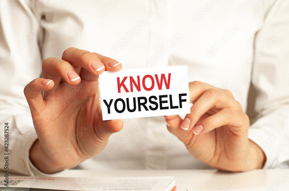 A woman in a white shirt holds a piece of paper with the text: know yourself. Business concept.