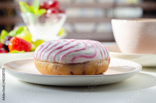 Delicious doughnut topped with white and pink icing served with coffee and fresh fruits