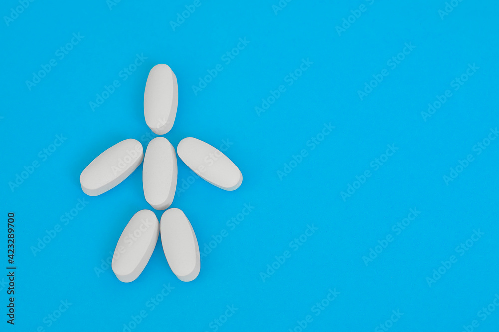 Small human figure laid out from white oblong pills on blue background. Human skeleton. Small human figure laid out from white oblong pills on blue background. Human skeleton.