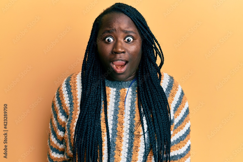 Young black woman with braids wearing casual winter sweater afraid and shocked with surprise and amazed expression, fear and excited face. Young black woman with braids wearing casual winter sweater afraid and shocked with surprise and amazed expression, fear and excited face.