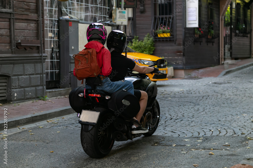 Two young people riding a motorcycle down the city street. Convenient mode of transport for tourists to visit popular places. Travel concept. Urban traffic road for people leisure travelling theme