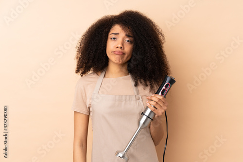 Young african american woman using hand blender isolated on beige background pleading