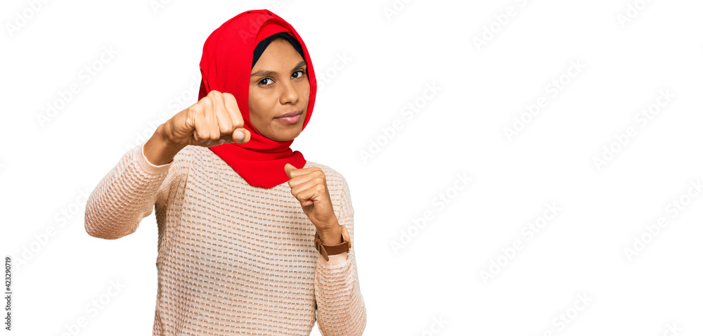 Fototapeta premium Young african american woman wearing traditional islamic hijab scarf punching fist to fight, aggressive and angry attack, threat and violence