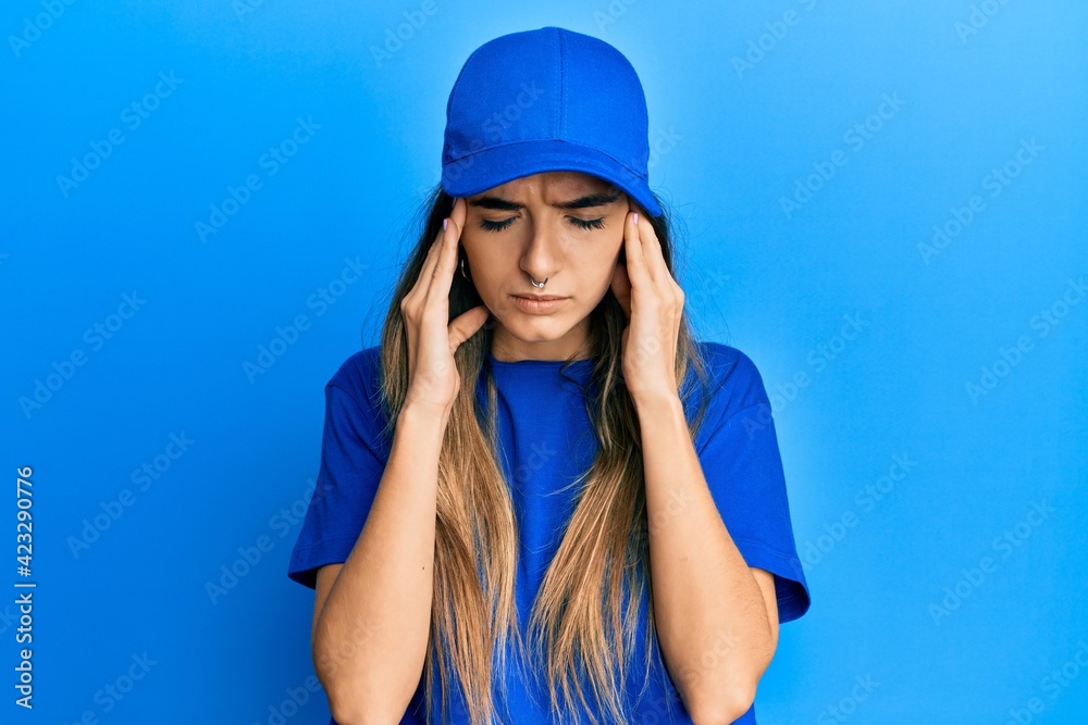 Young hispanic woman wearing delivery uniform and cap suffering from headache desperate and stressed because pain and migraine. hands on head.