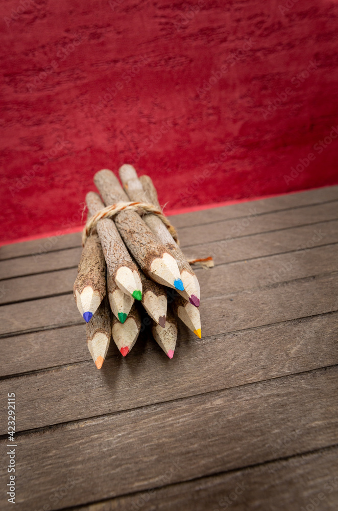 Naklejka premium bound crayons made of untreated, real wood, unique and with real tree bark on a wooden board and red background for nature topics, students and artists