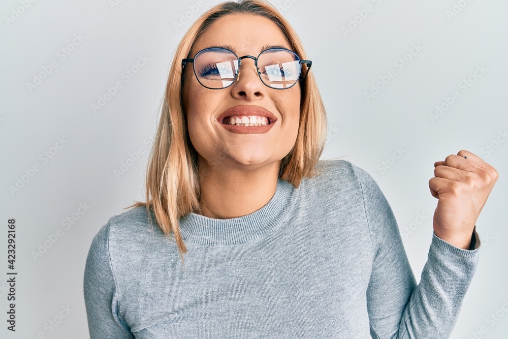 Young caucasian woman wearing casual clothes and glasses screaming proud, celebrating victory and success very excited with raised arm