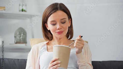 Young pregnant woman holding ice cream and spoon at home