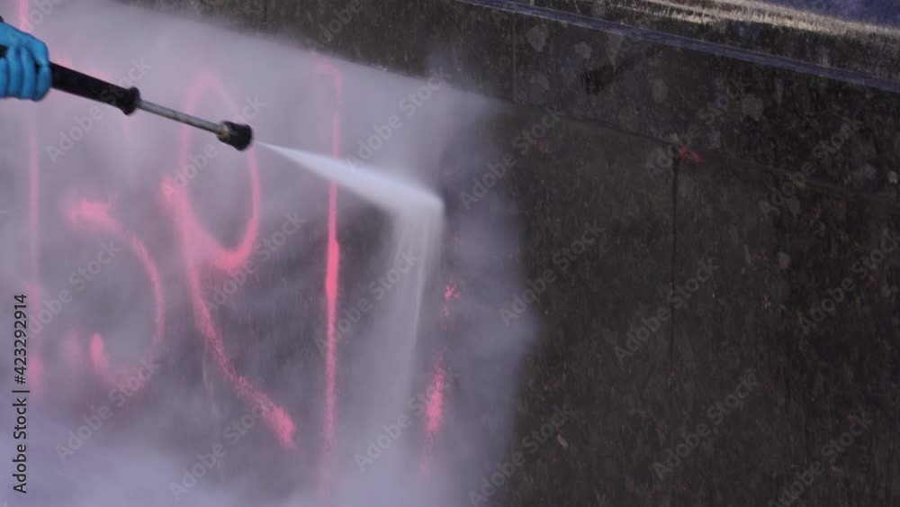 The specialist cleans the stone surface of the street from paint and dirt. A cleaner in protective clothing washes the contaminated area with a jet of water. Professional removal of graffiti