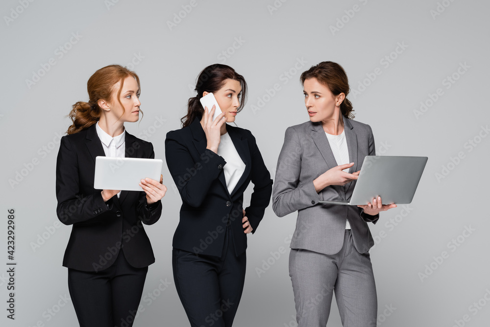 Businesswomen in formal wear using gadgets isolated on grey Businesswomen in formal wear using gadgets isolated on grey