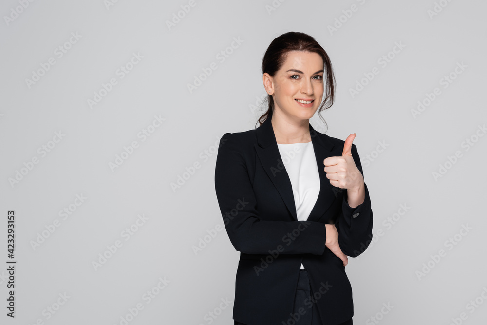 Smiling businesswoman in suit showing like gesture isolated on grey Smiling businesswoman in suit showing like gesture isolated on grey