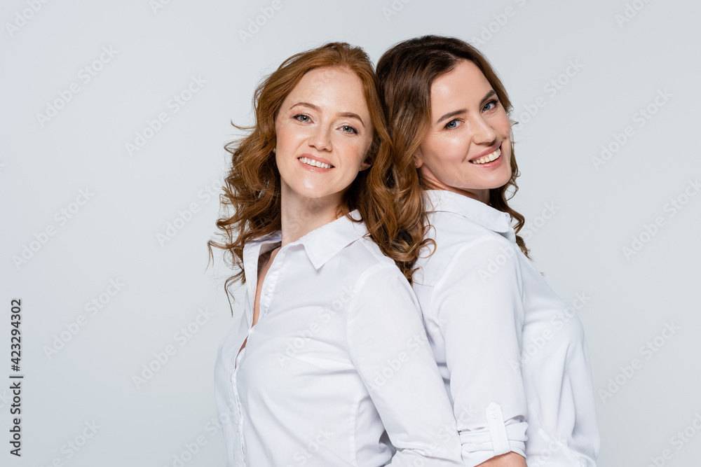 Smiling women standing back to back isolated on grey Smiling women standing back to back isolated on grey