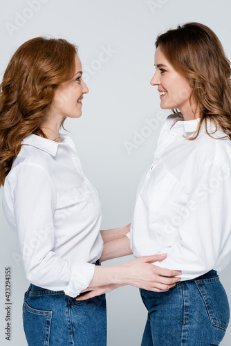 Side view of women smiling at each other isolated on grey