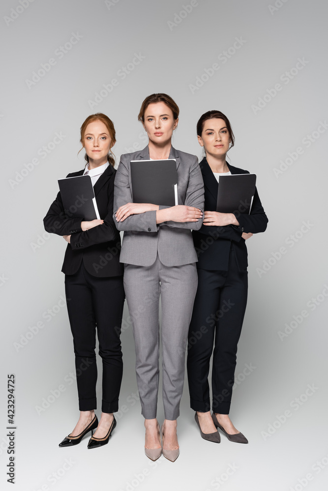 Confident businesswomen with paper folders standing on grey background Confident businesswomen with paper folders standing on grey background