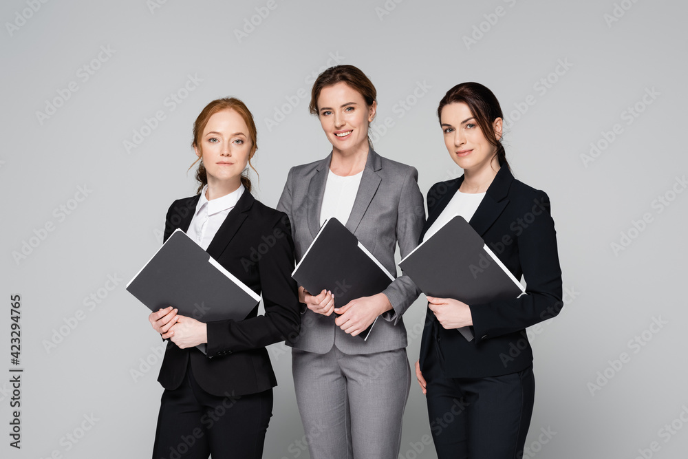 Positive businesswomen holding paper folders isolated on grey Positive businesswomen holding paper folders isolated on grey