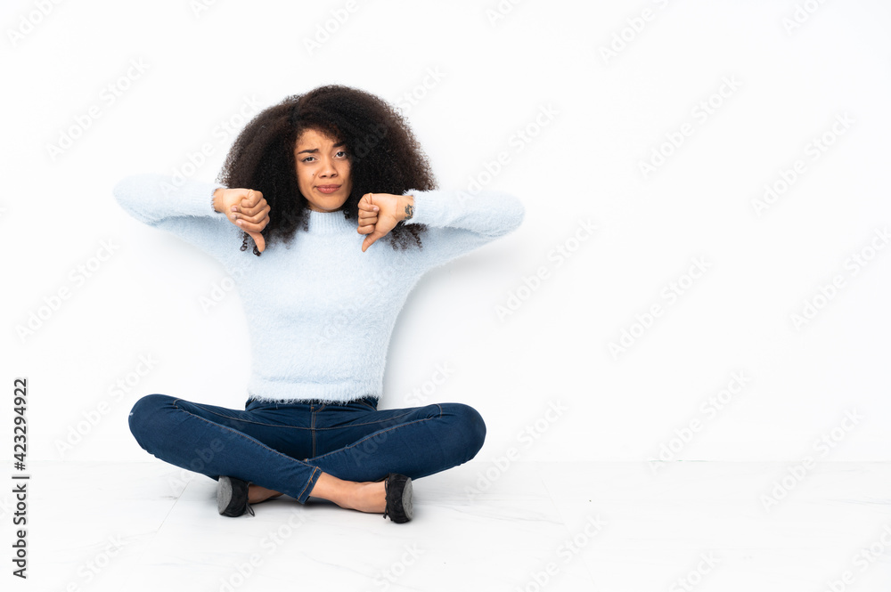 Young african american woman sitting on the floor showing thumb down Young african american woman sitting on the floor showing thumb down
