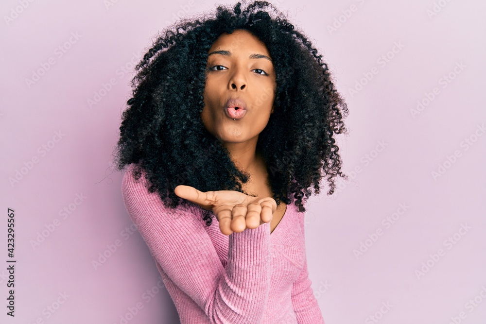African american woman with afro hair wearing casual pink shirt looking at the camera blowing a kiss with hand on air being lovely and sexy. love expression. African american woman with afro hair wearing casual pink shirt looking at the camera blowing a kiss with hand on air being lovely and sexy. love expression.