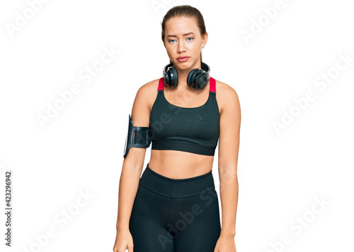 Beautiful blonde woman wearing gym clothes and using headphones looking sleepy and tired, exhausted for fatigue and hangover, lazy eyes in the morning.