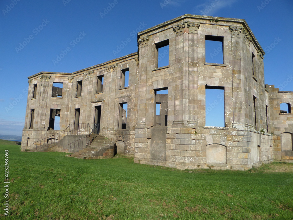 Downhill House Herrenhaus. Fassade einer steinernen Ruine. Der blaue Himmel ist durch die Fensterlöcher hindurch zu sehen. Altes zerfallenes Gebäude auf grünem Rasen. Downhill House Herrenhaus. Fassade einer steinernen Ruine. Der blaue Himmel ist durch die Fensterlöcher hindurch zu sehen. Altes zerfallenes Gebäude auf grünem Rasen.