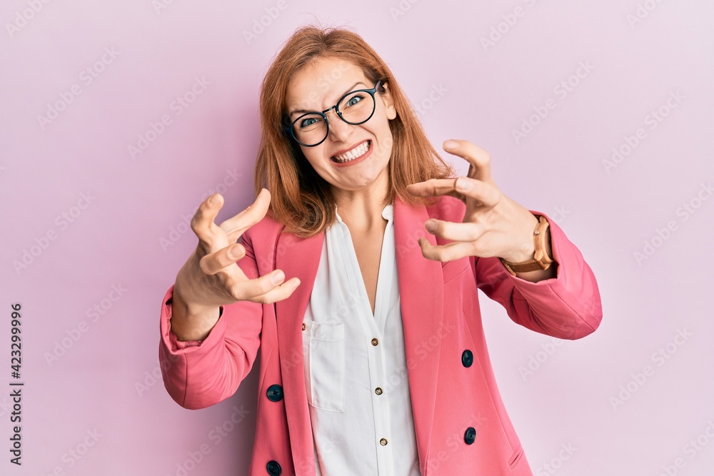 Young caucasian woman wearing business style and glasses shouting frustrated with rage, hands trying to strangle, yelling mad