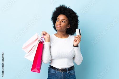 Young African American woman isolated on blue background holding shopping bags and a credit card and thinking
