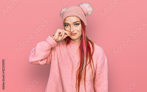 Young caucasian woman wearing casual clothes and wool cap mouth and lips shut as zip with fingers. secret and silent, taboo talking