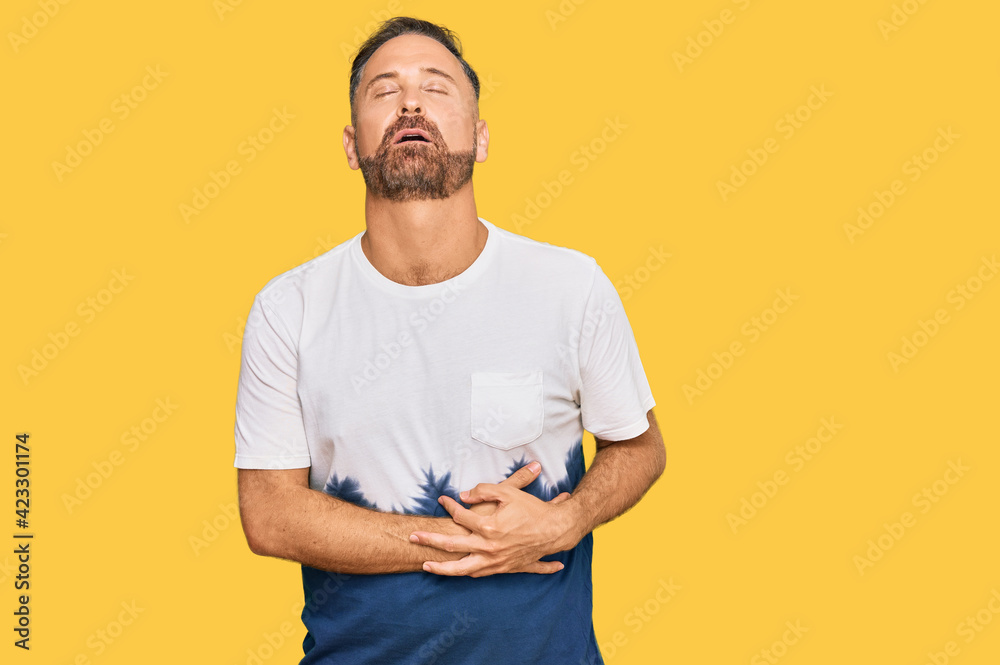 Handsome middle age man wearing casual tie dye tshirt with hand on stomach because nausea, painful disease feeling unwell. ache concept. Handsome middle age man wearing casual tie dye tshirt with hand on stomach because nausea, painful disease feeling unwell. ache concept.