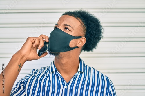Young african american man wearing medical mask talking on the smartphone at the city.