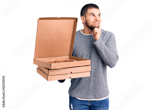 Young handsome man holding delivery italian pizza boxes serious face thinking about question with hand on chin, thoughtful about confusing idea photo