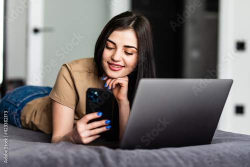 Young pretty woman use phone and laptop sitting on the bed