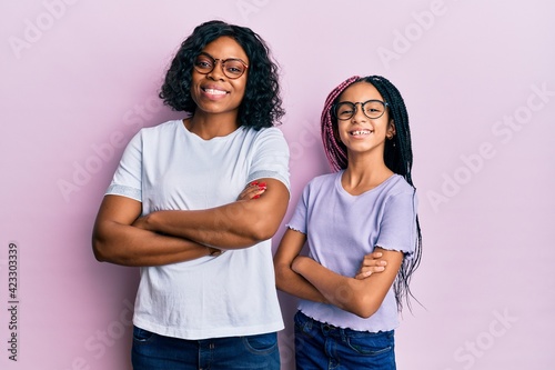 Beautiful african american mother and daughter wearing casual clothes and glasses happy face smiling with crossed arms looking at the camera. positive person.