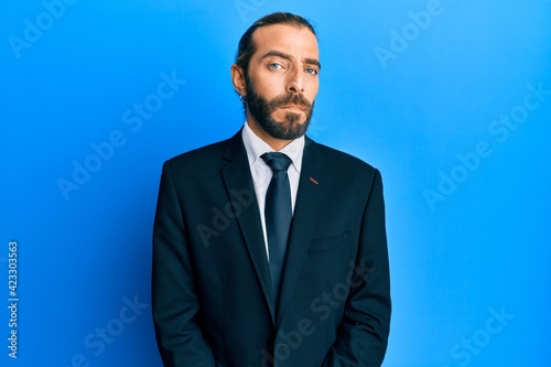 Attractive man with long hair and beard wearing business suit and tie with serious expression on face. simple and natural looking at the camera.