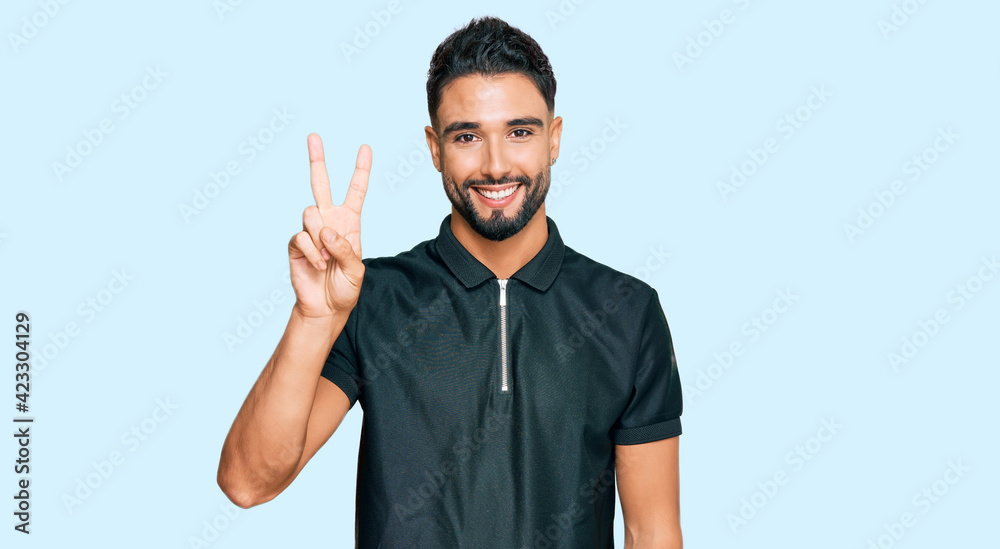 Fototapeta premium Young man with beard wearing sportswear showing and pointing up with fingers number two while smiling confident and happy.