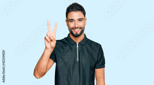 Young man with beard wearing sportswear showing and pointing up with fingers number two while smiling confident and happy.