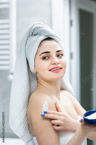 Portrait of woman in bathroom applying moisturizing cream in bathroom after shower